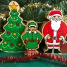 A chunky wooden green elf toy figure standing next to Father Christmas and Christmas tree